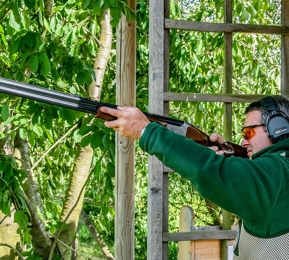 A man in protective gear aiming a shotgun