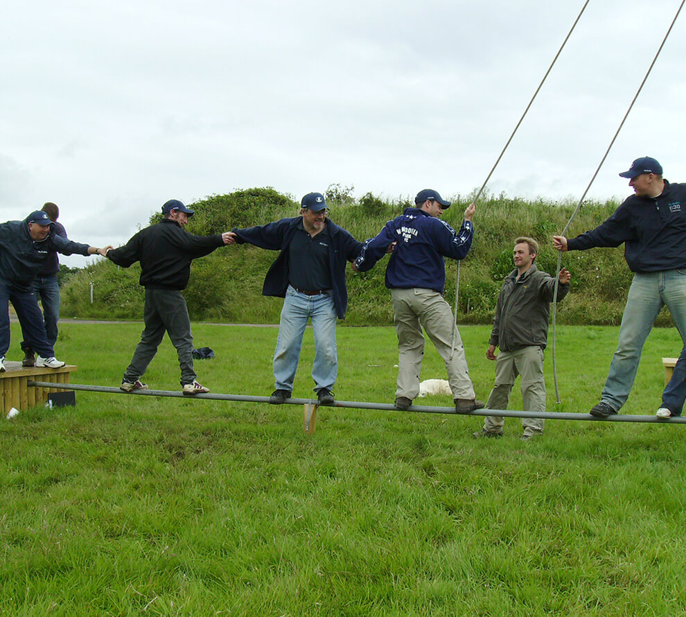 A group working together to try and balance on a thin piece of metal