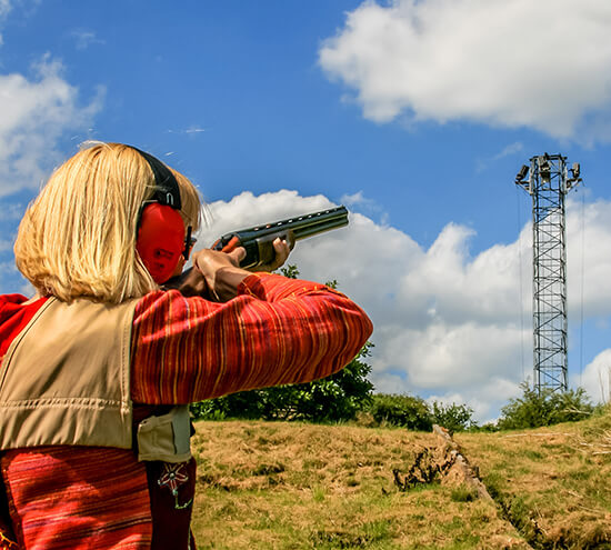 A woman aiming a shotgun across a field