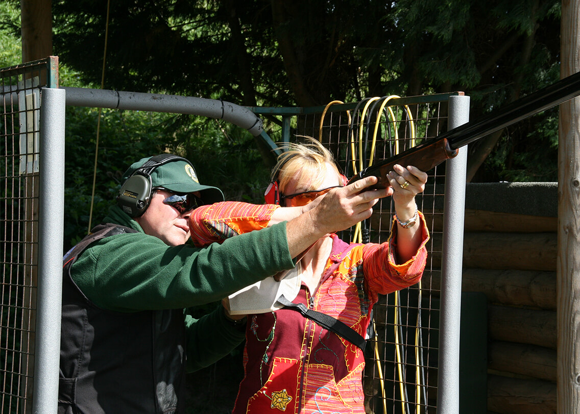 A woman being taught how to shoot a shotgun