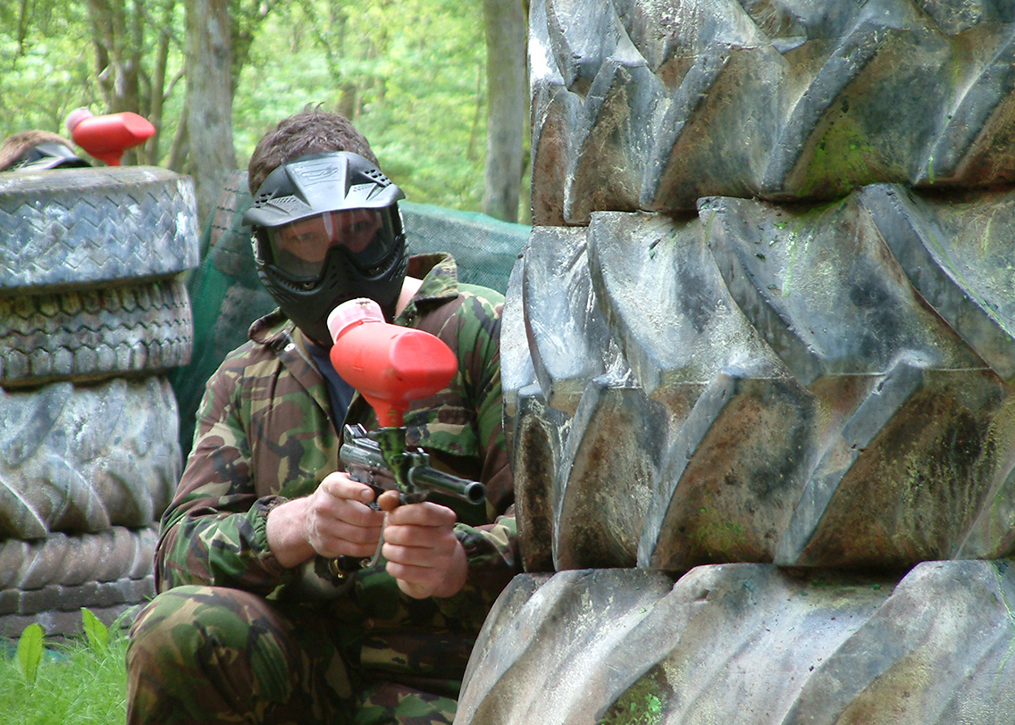 A man hiding behind some large tyres in a paintball match