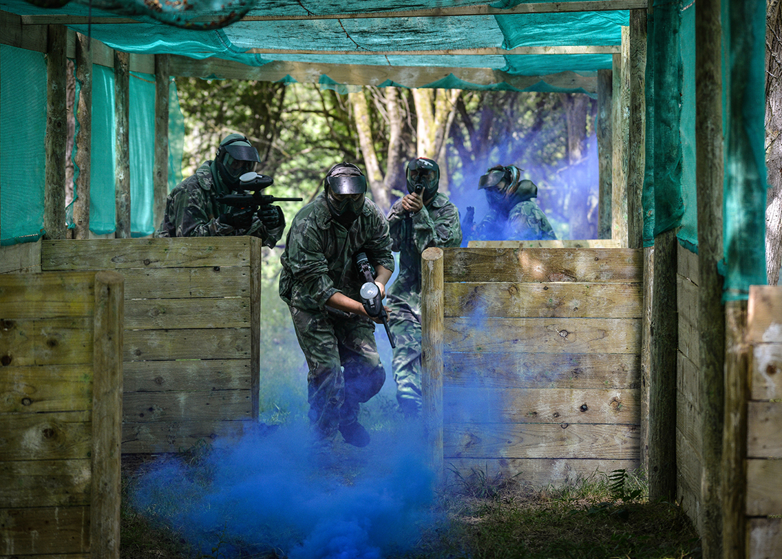 A man hiding behind some large tyres in a paintball match
