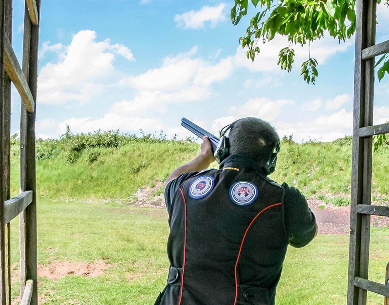 A man aiming down a range with a shotgun